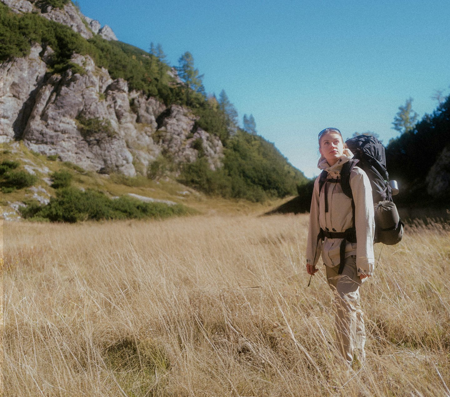 A woman is standing in a meadow while trekking in the mountains.