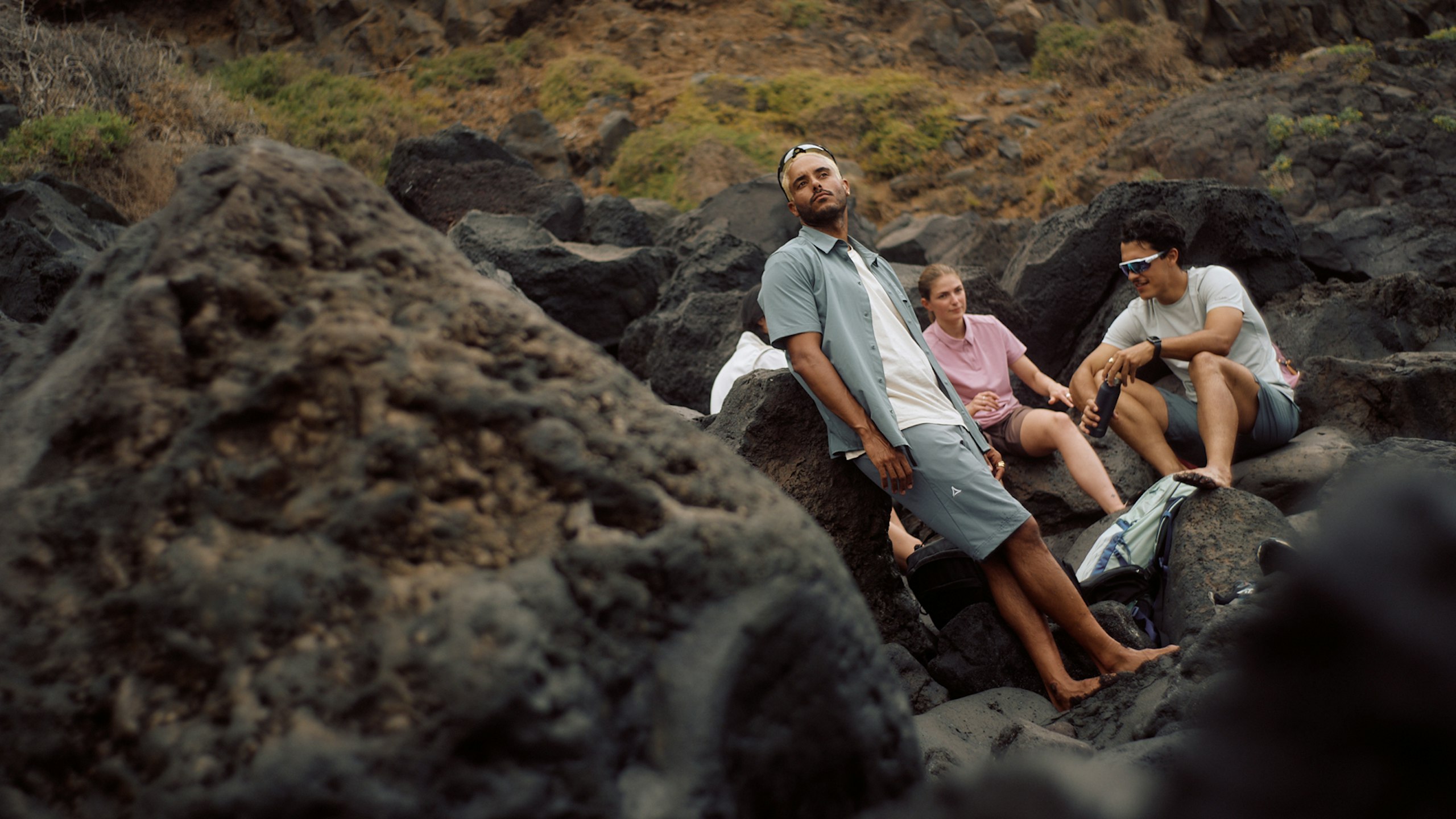 drei Personen sitzend und stehend in der Natur in Wanderoutfits