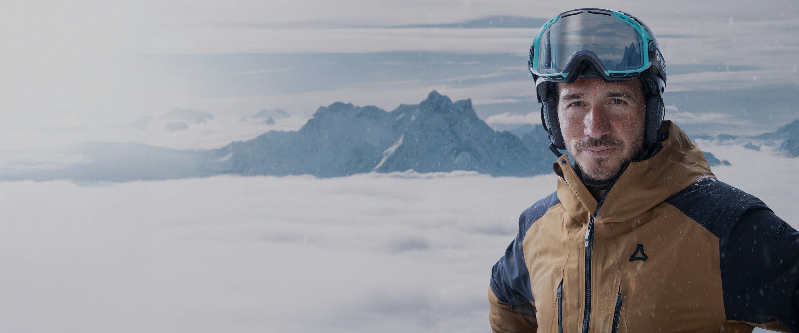 Ein Mann in Ski Bekleidung vor einem verschneiten Bergpanorama, Schöffel.