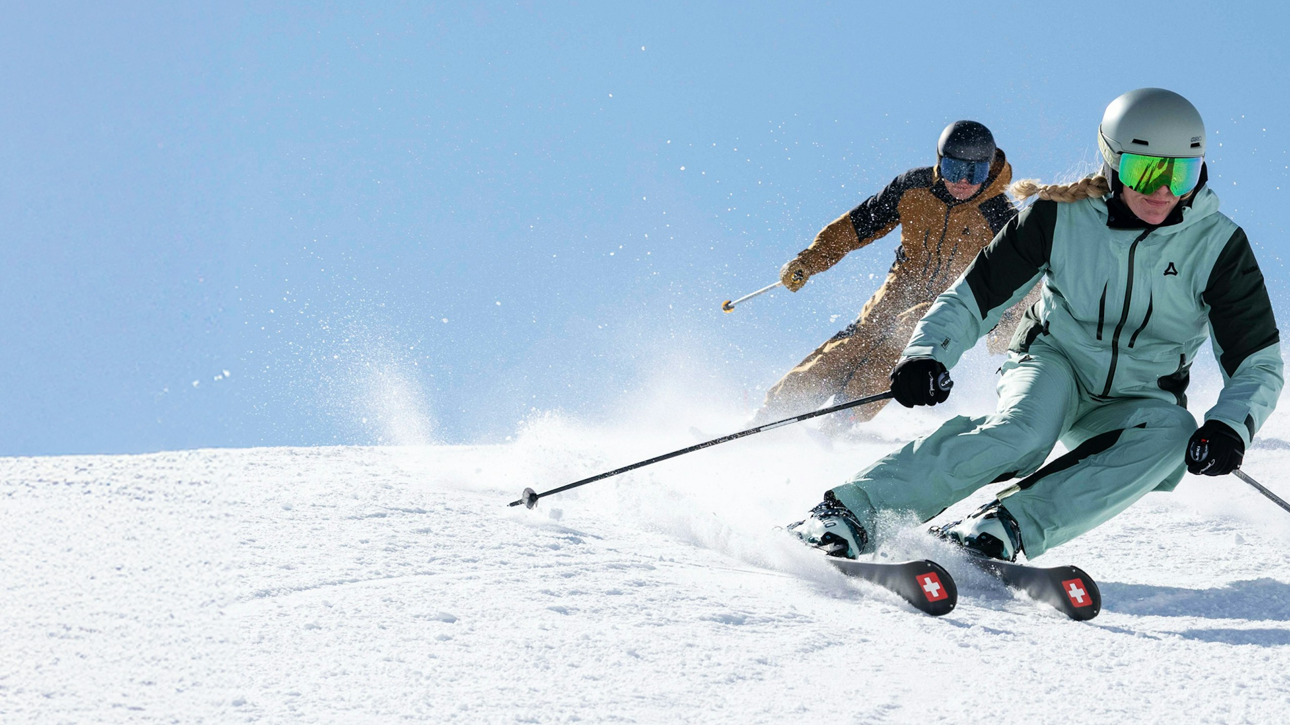 Zwei Personen fahren mit Skiern einen Berg hinunter, Schöffel.
