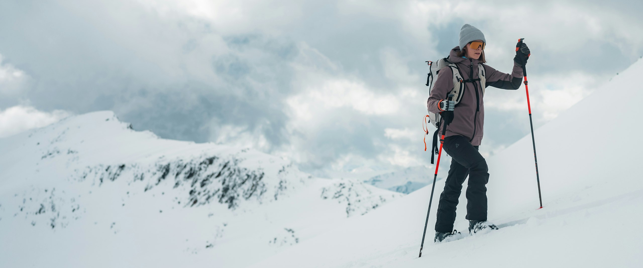 Eine Frau läuft mit Skiern einen schneebedeckten Berg hinauf, Schöffel.