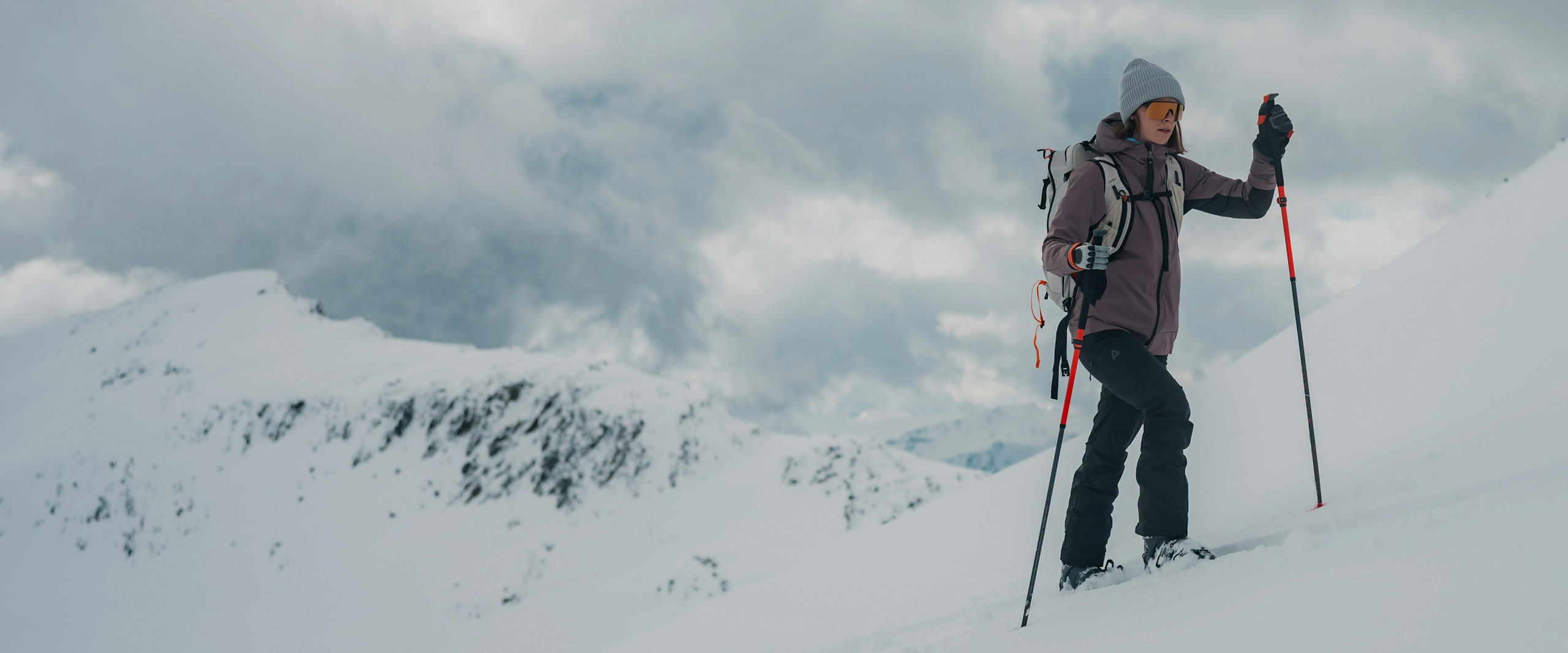 Eine Frau läuft mit Skiern einen schneebedeckten Berg hinauf, Schöffel.