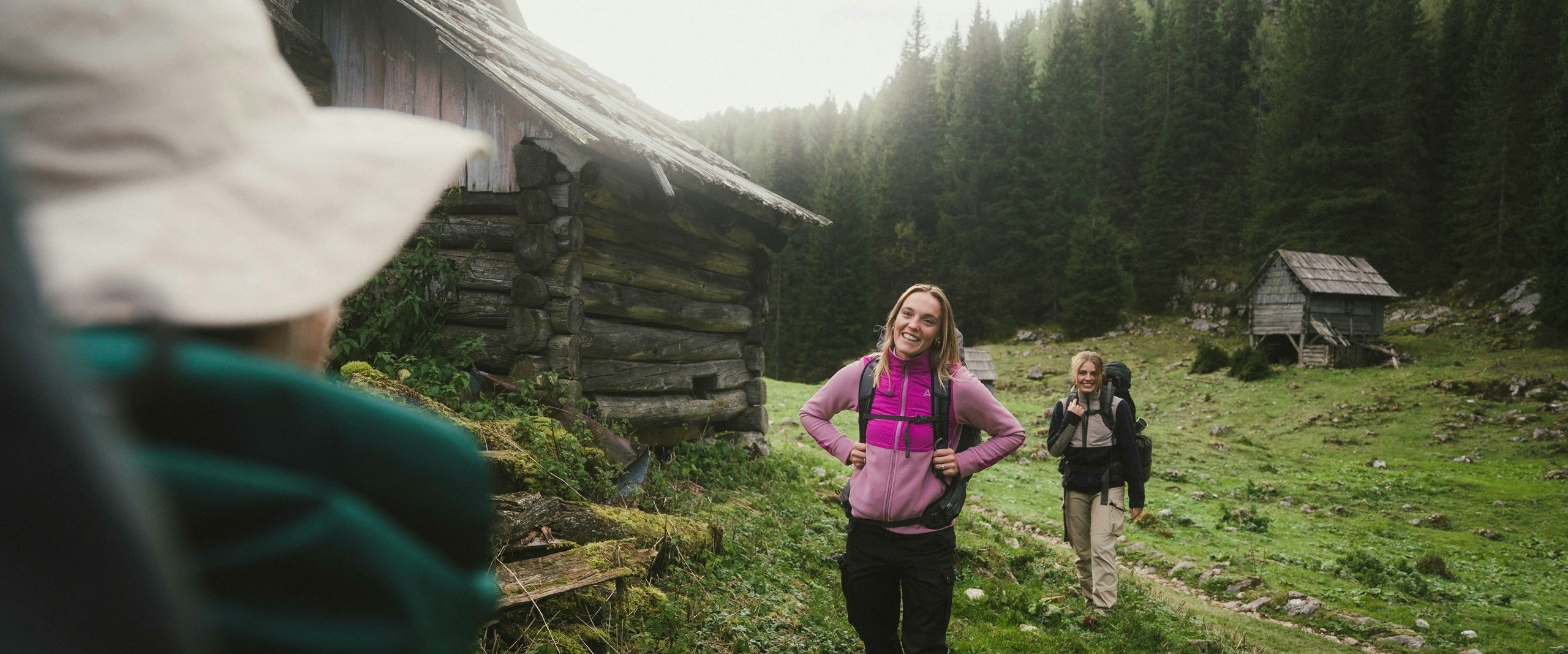 Two people walk past a hut during a mountain hike.