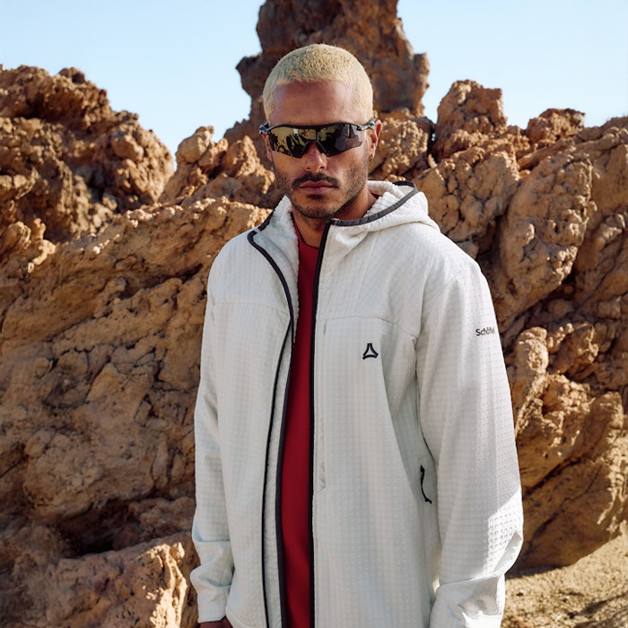 Mann in weißem Fleece, rotes Shirt und Sonnenbrille im Sommer schaut frontal in Kamera - Wanderung