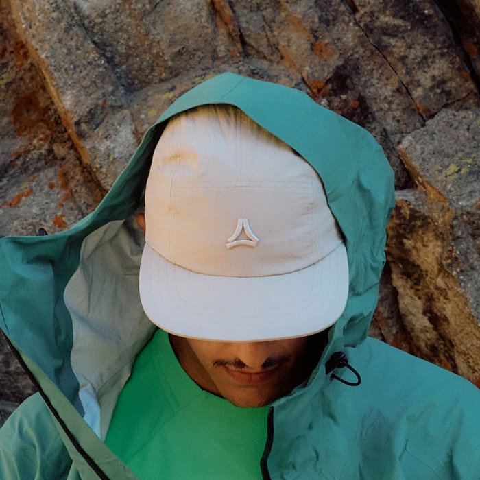 Mann in grünem Shirt trägt weiße Cap schaut runter und trägt eine grüne Jacke