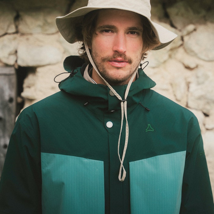 A man in a green trekking jacket is wearing a beige sun hat.