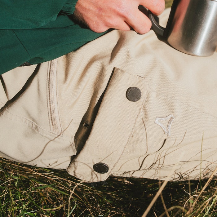 The closed outer pocket of a pair of beige trekking trousers can be seen. 