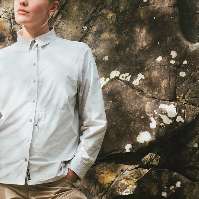 Lady in front of stone wall wearing a light-coloured trekking blouse.