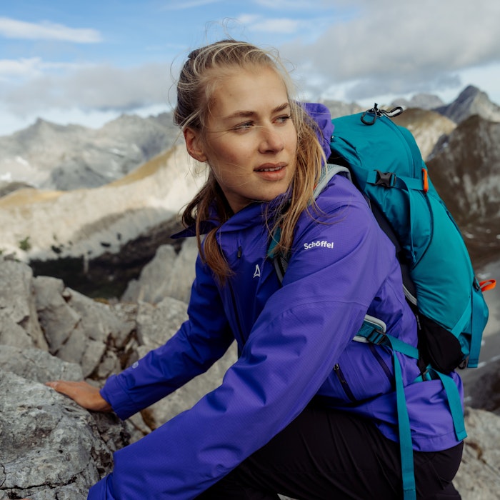 Softshelljacke waschen, blonde Frau in lila-blauer Schöffel Softshacke klettert auf einem Berg, Schöffel.