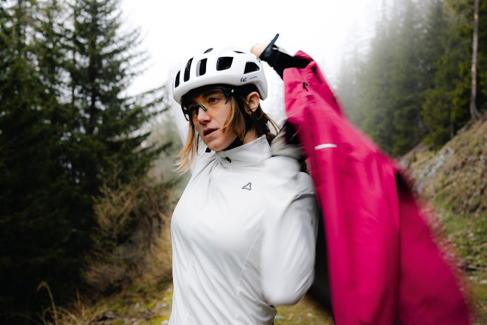 Une femme vêtue d'un t-shirt blanc enfile une veste de cycliste rose, Schöffel.