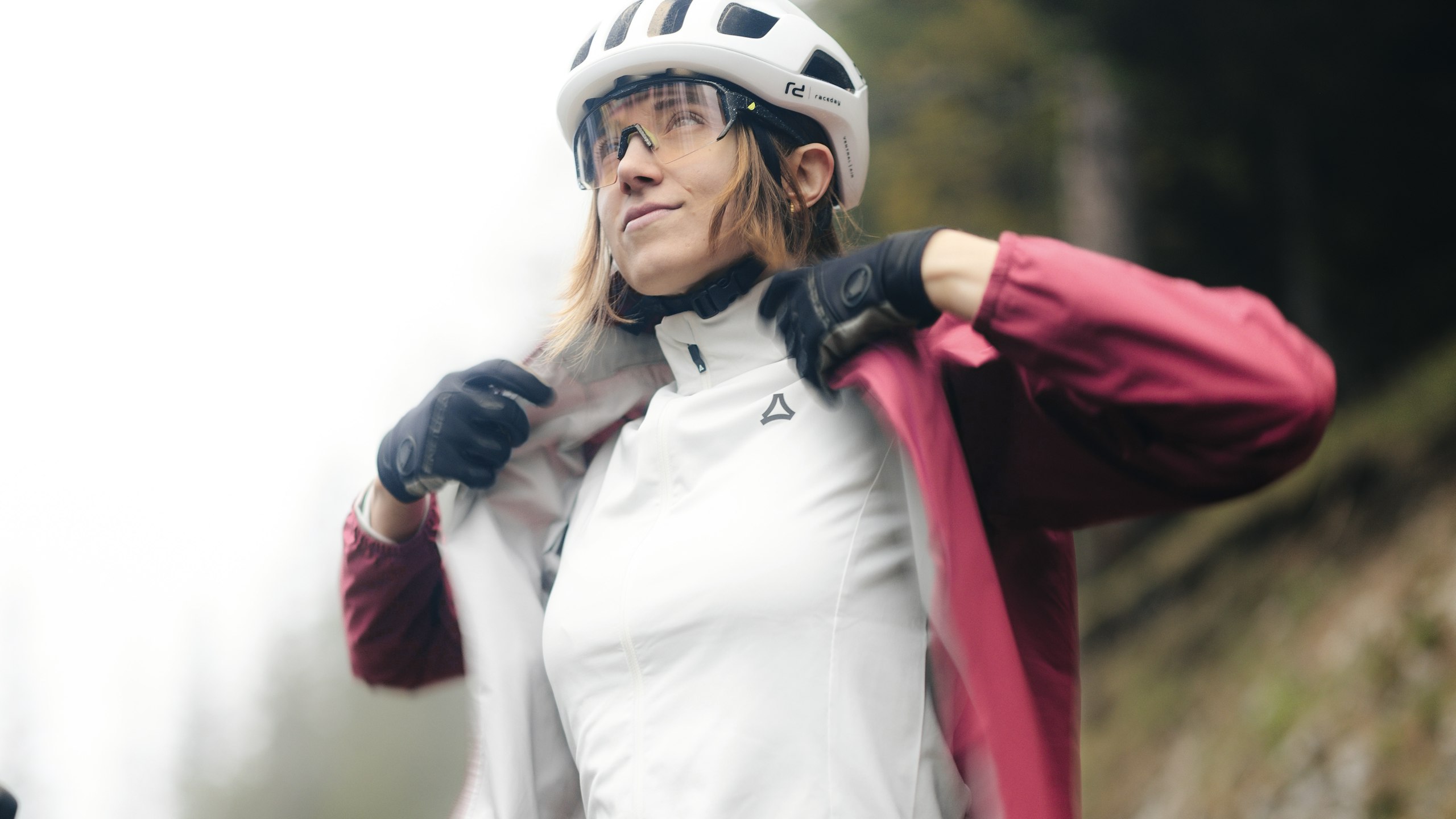 Une femme assise sur un vélo, vêtue d'un t-shirt blanc, ferme sa veste de cycliste rose, Schöffel.