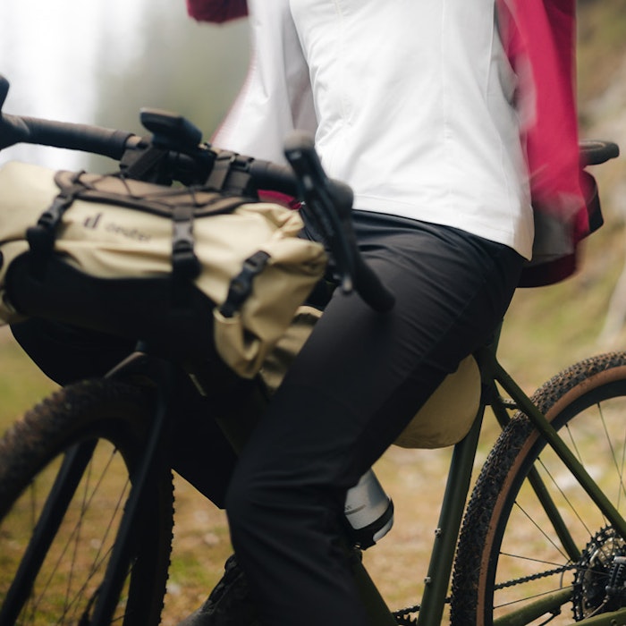 Une femme à vélo se tient sur un chemin de campagne et ferme sa veste de cycliste rose, Schöffel.